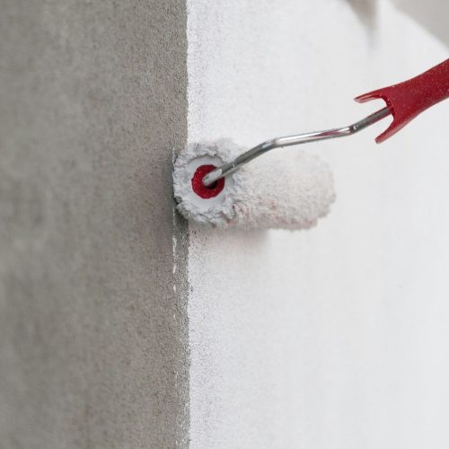 paint-roller-being-used-with-white-paint-on-a-gray-RJWGGRP